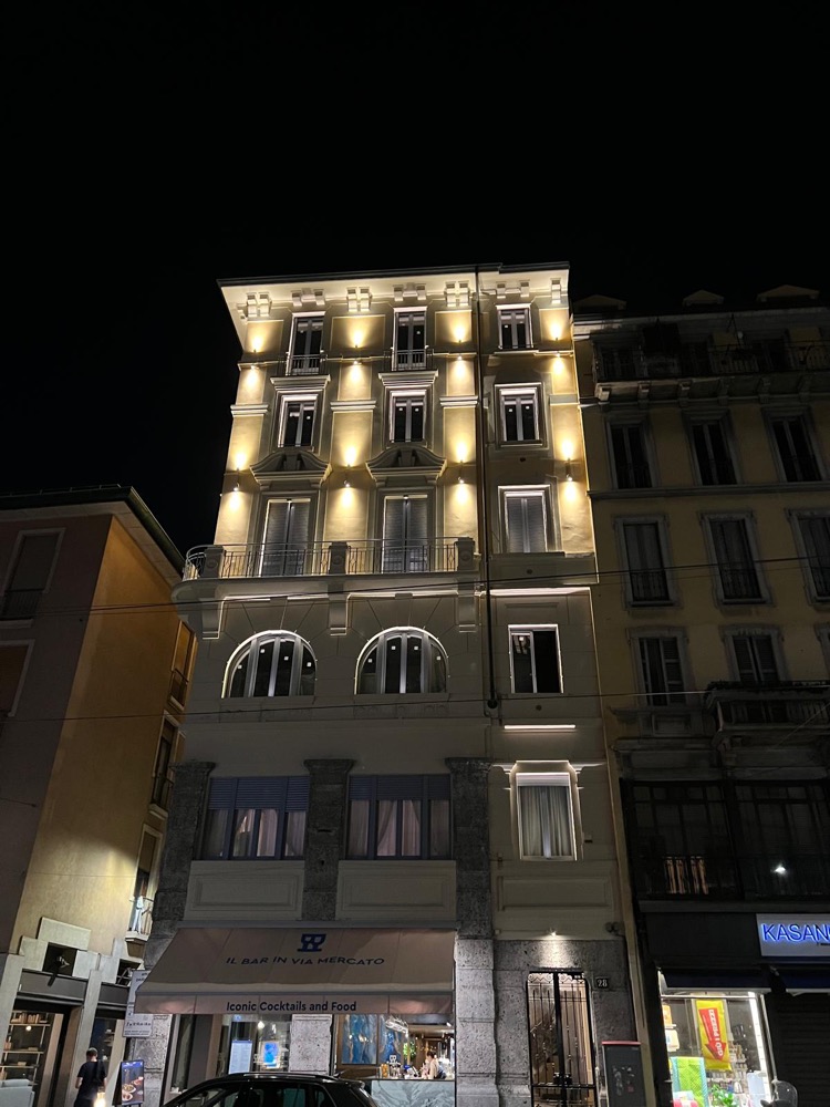 The illuminated façade and entrance of the apartment building at Via Mercato 28, Milan, photographed at night